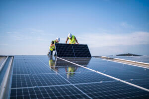 Team of two engineers installing solar panels on industrial factory roof.