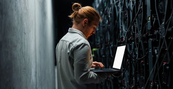 IT-Mitarbeiter bedient einen Laptop neben Serverracks in einem Rechenzentrum